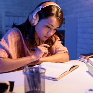Teen girl wears headphones and reads over notes to develop good study skills and habits. 